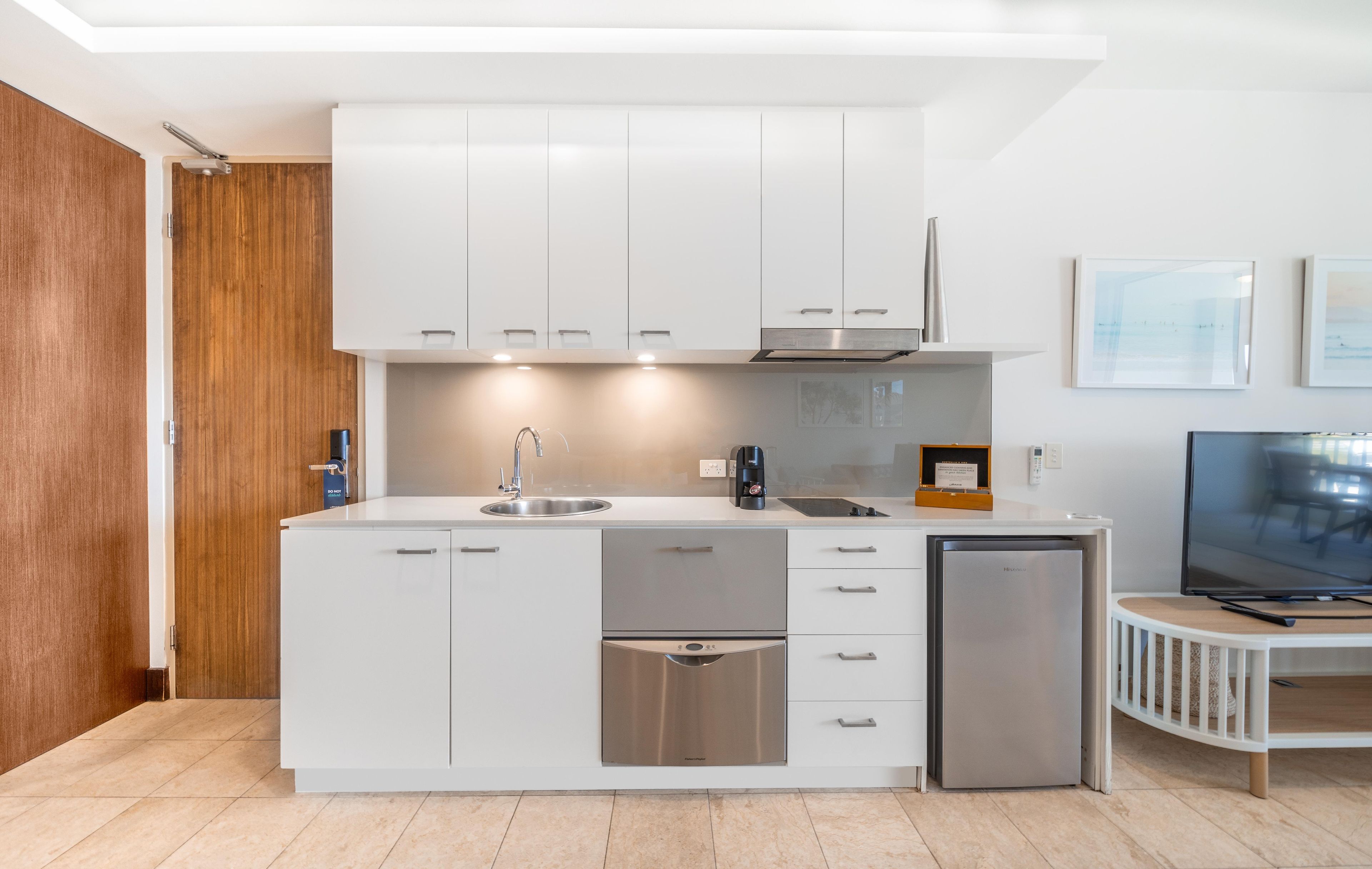 A modern kitchen with white cabinetry, a built-in dishwasher, and a compact refrigerator.
