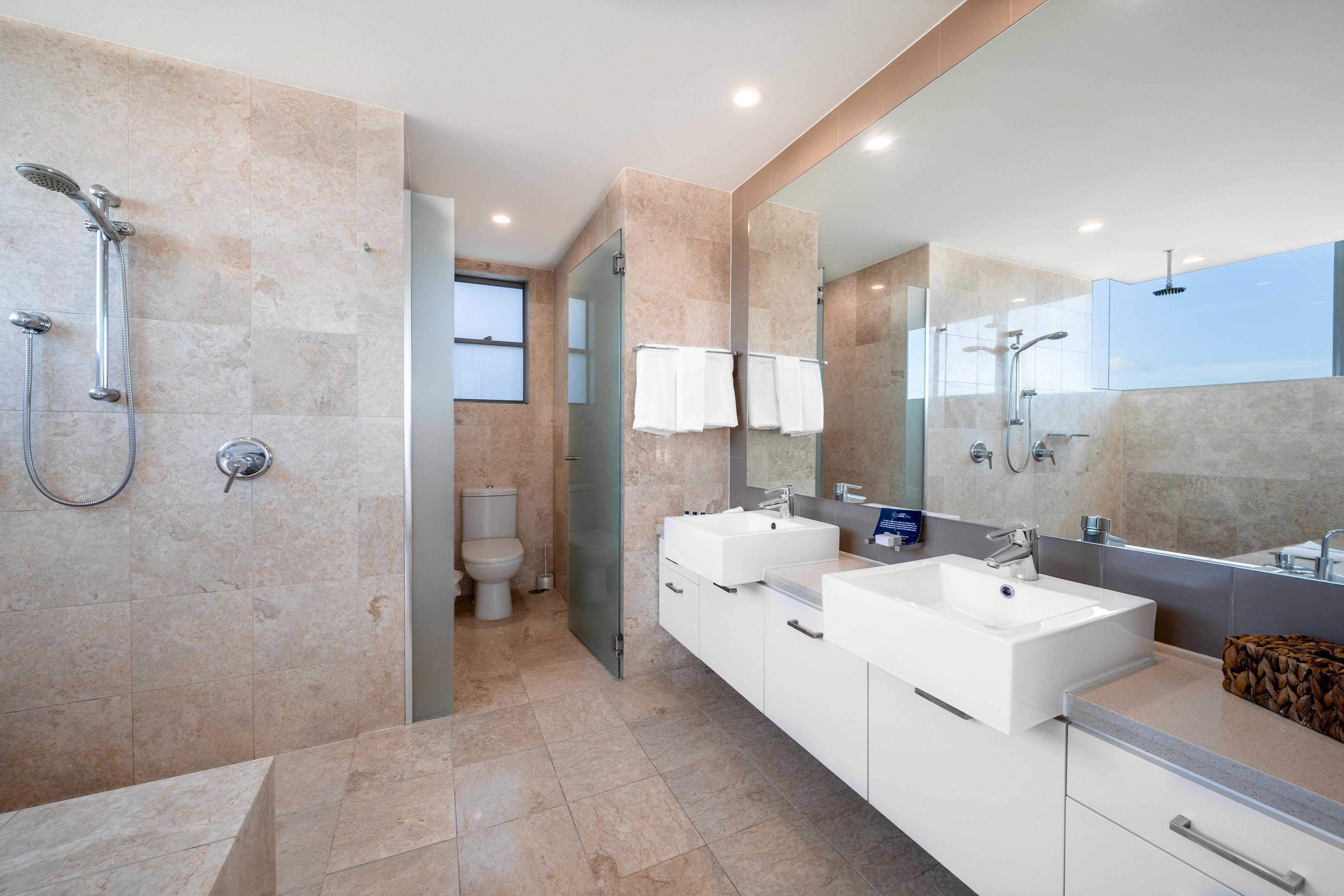 A modern bathroom with a glass shower enclosure, a toilet, and a vanity with two sinks.
