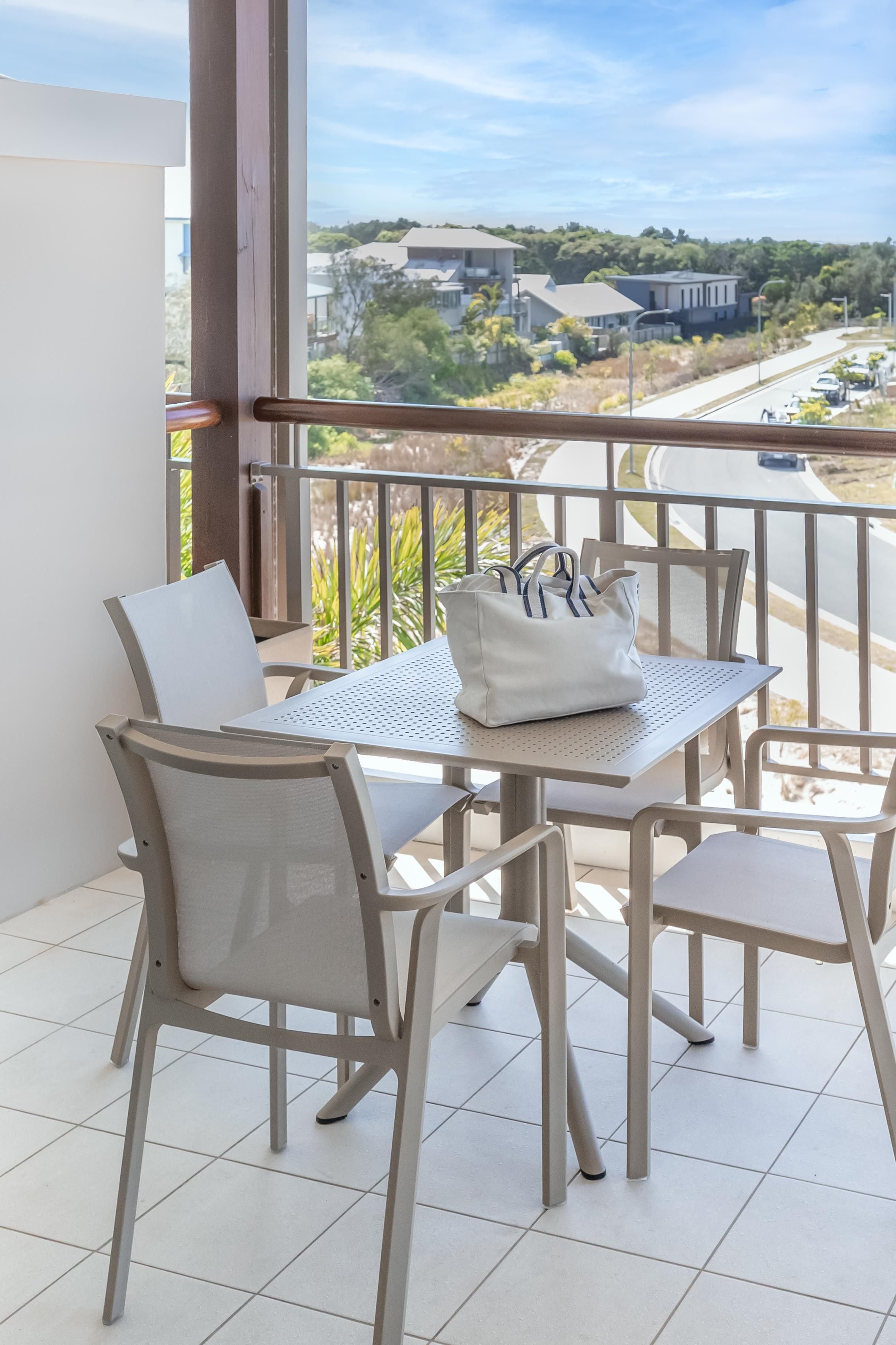 A balcony with a table and chairs, a white bag, and a view of a road and buildings.