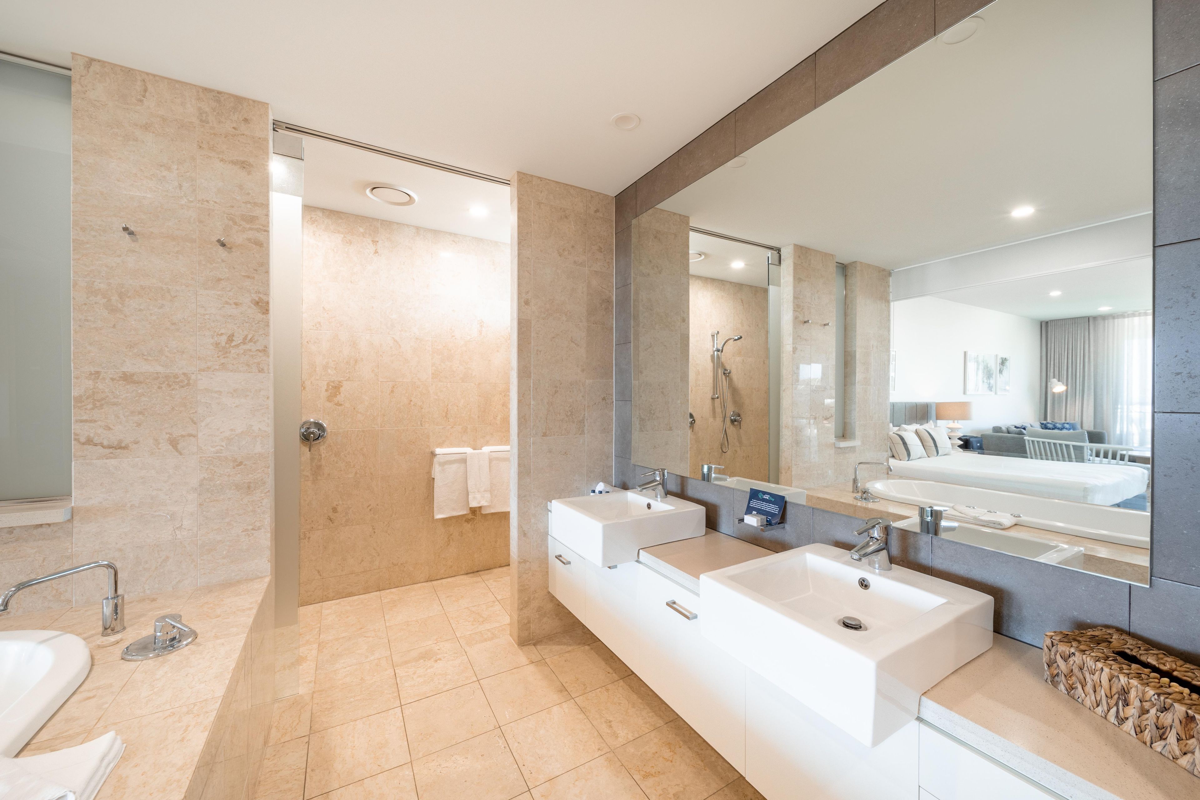 A modern bathroom with two sinks, a shower, and a large mirror.
