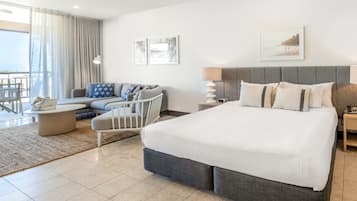 A modern hotel room with a large bed, a sofa, a chair, and a balcony with curtains.