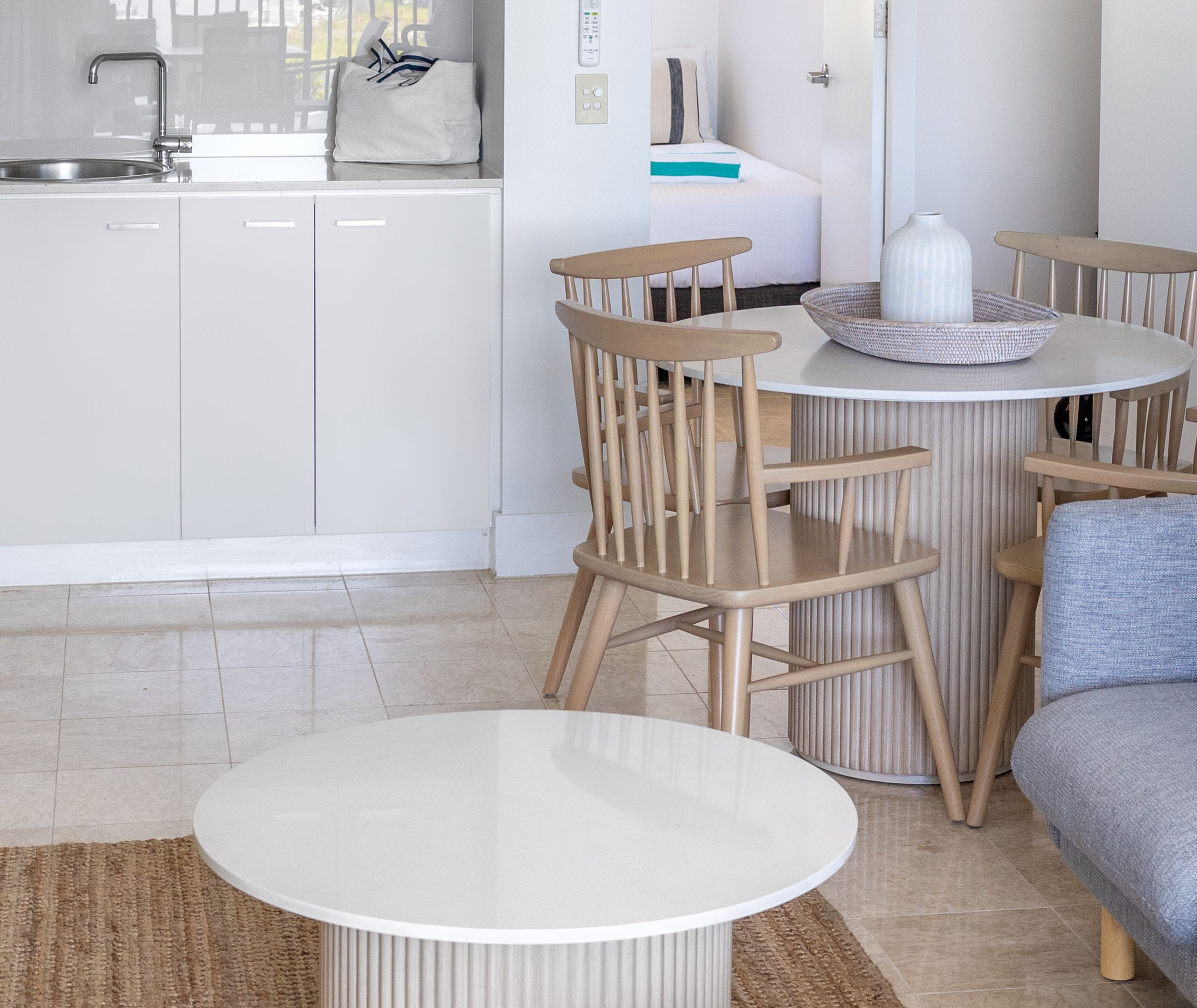 A modern kitchen with white cabinets, a stainless steel sink, and a dining area with a round table and wooden chairs.