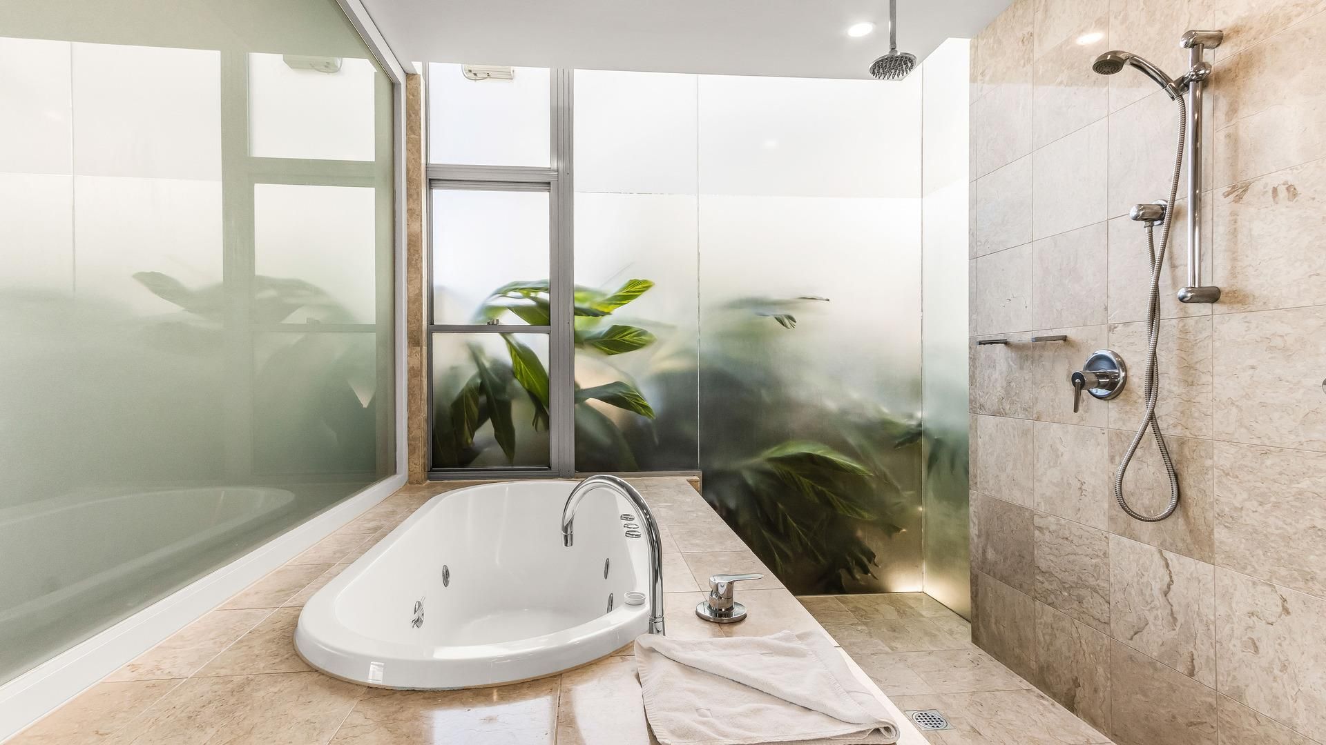 Une salle de bain moderne avec une baignoire sur pieds, une douche en verre et une vue sur la verdure à travers un vitrage dépoli.