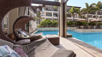 A poolside area with wicker lounge chairs, a small pool, and a view of a multi-story building with balconies.