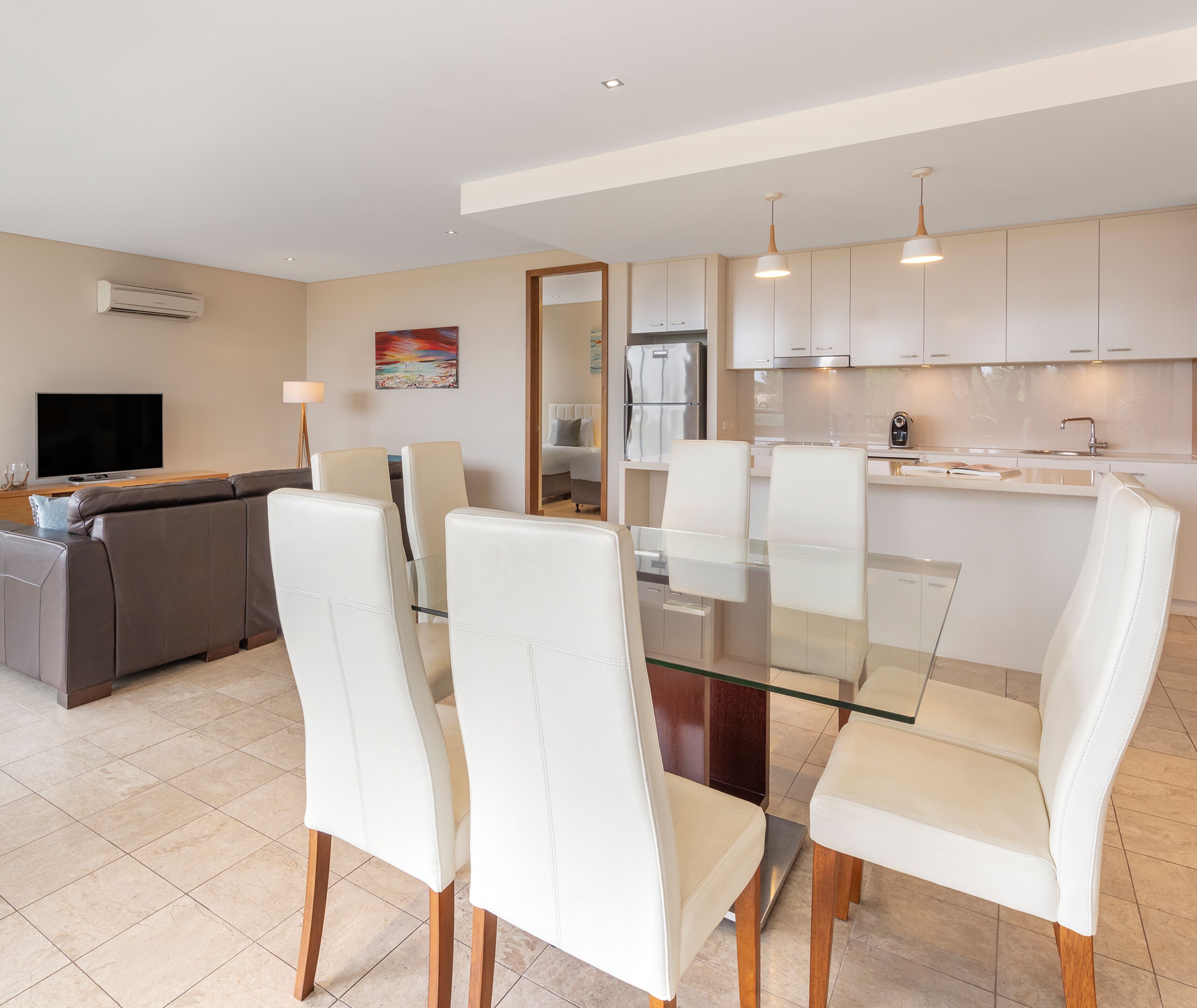 A modern kitchen with white cabinets, a glass dining table, and white chairs.