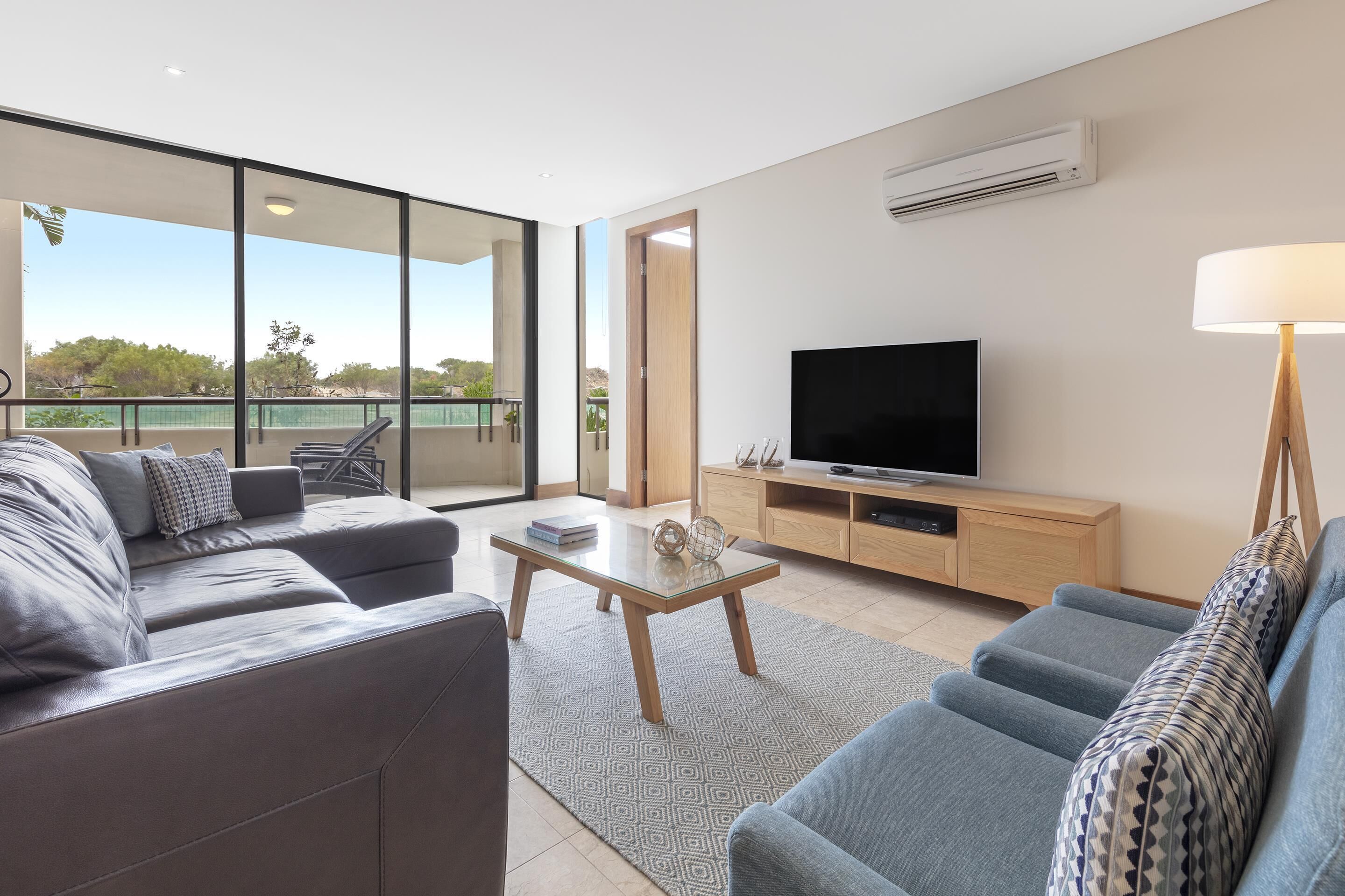 A modern living room with a sofa, a coffee table, a TV, and a balcony with a view.