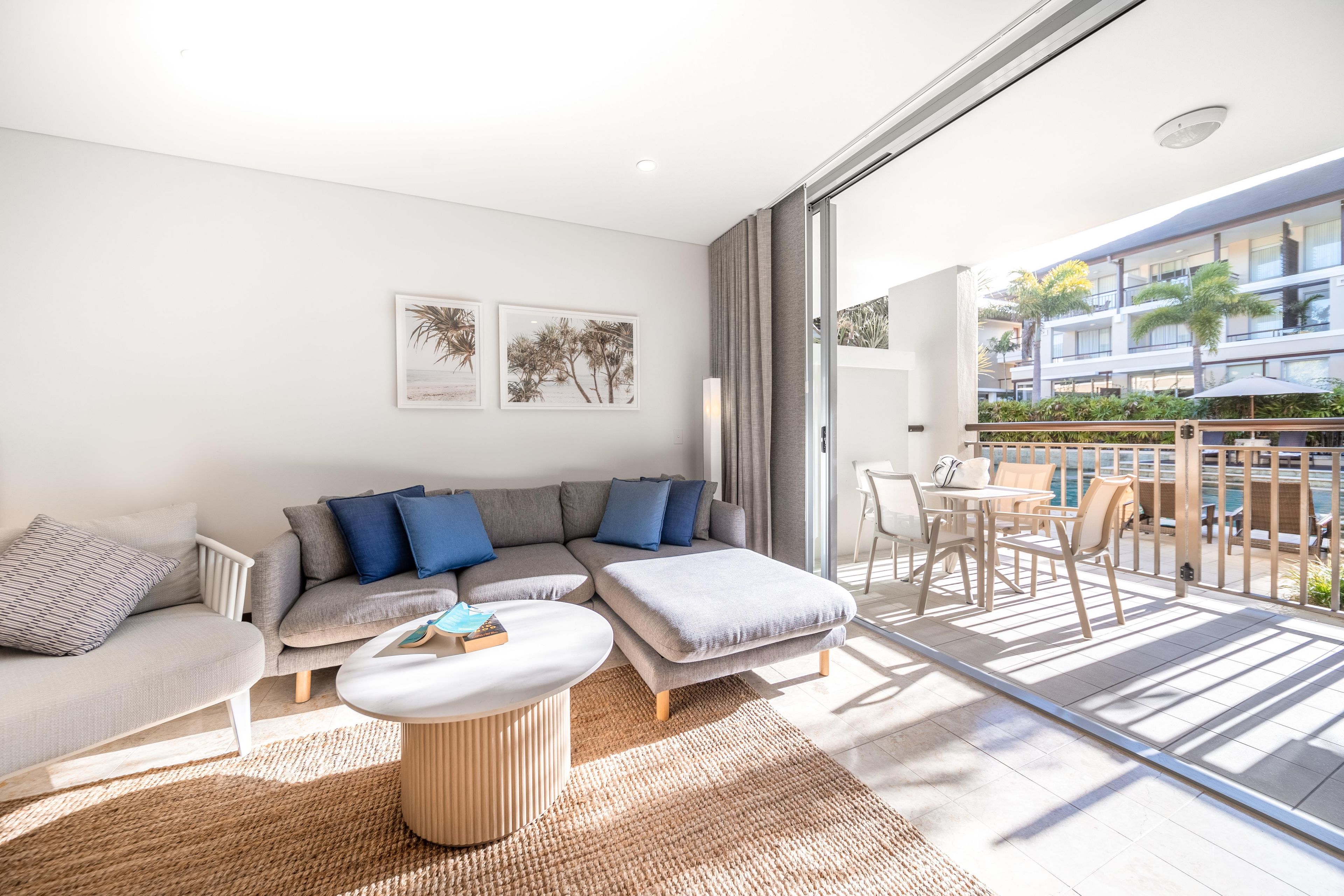 A modern living room with a sofa, armchairs, a coffee table, and a balcony with outdoor furniture.
