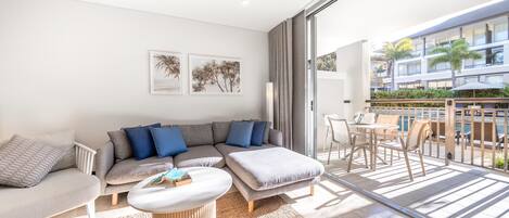 A modern living room with a sofa, armchairs, a coffee table, and a balcony with outdoor furniture.
