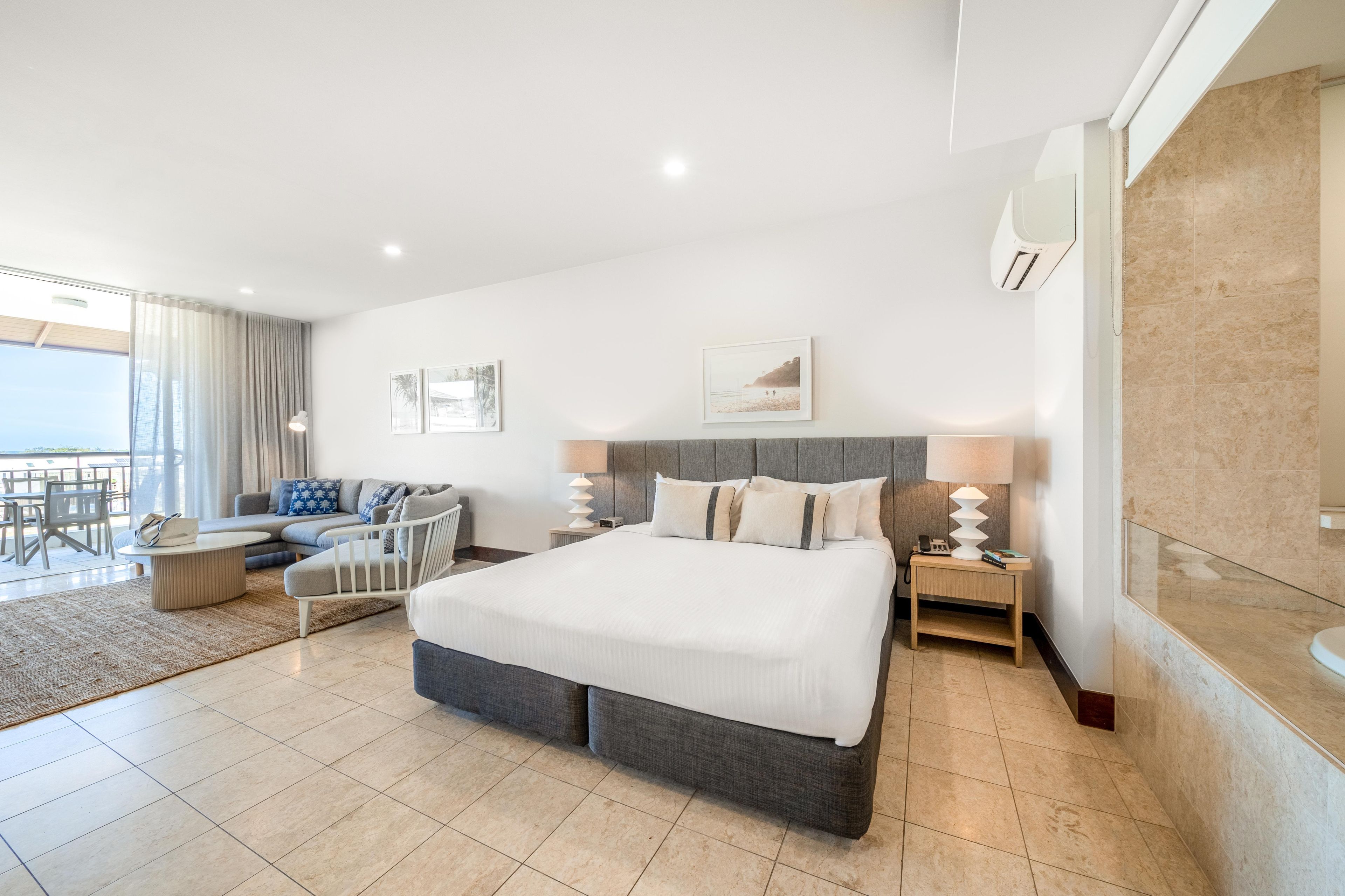 A hotel room with a large bed, a sofa, a dining area, and a balcony.