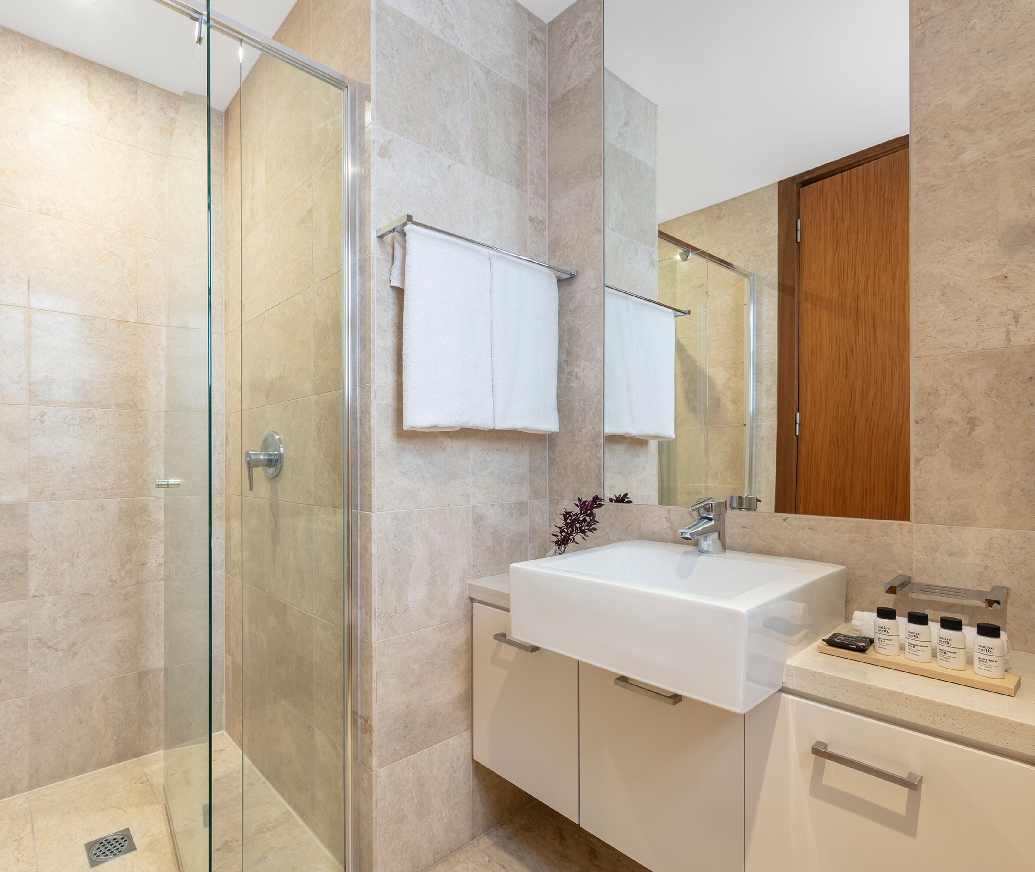 A modern bathroom with a glass shower enclosure, a white sink, and a wooden cabinet.