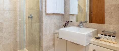 A modern bathroom with a glass shower enclosure, a white sink, and a wooden cabinet.