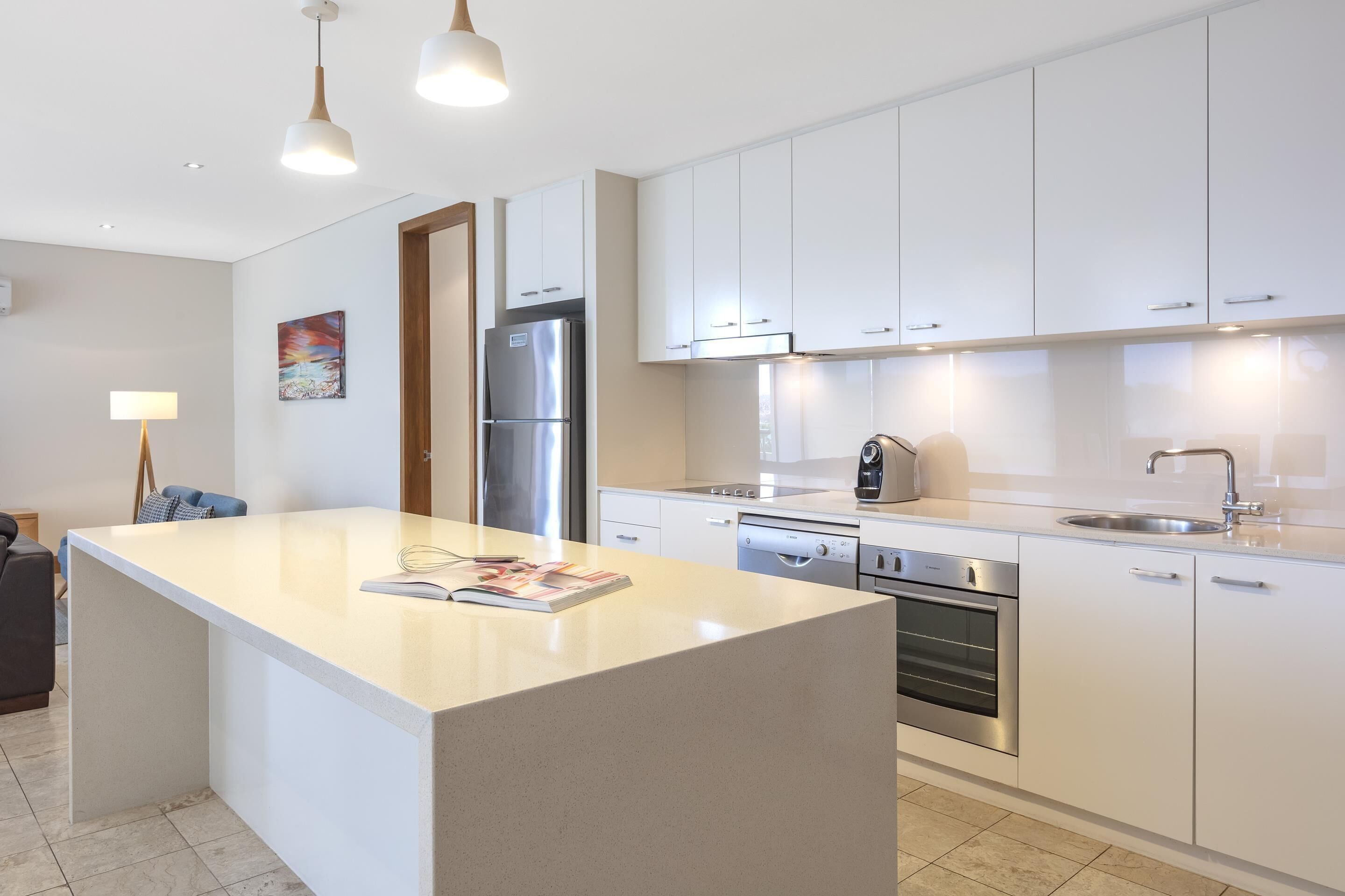 Une cuisine moderne avec des armoires blanches, des appareils en acier inoxydable et des luminaires suspendus.