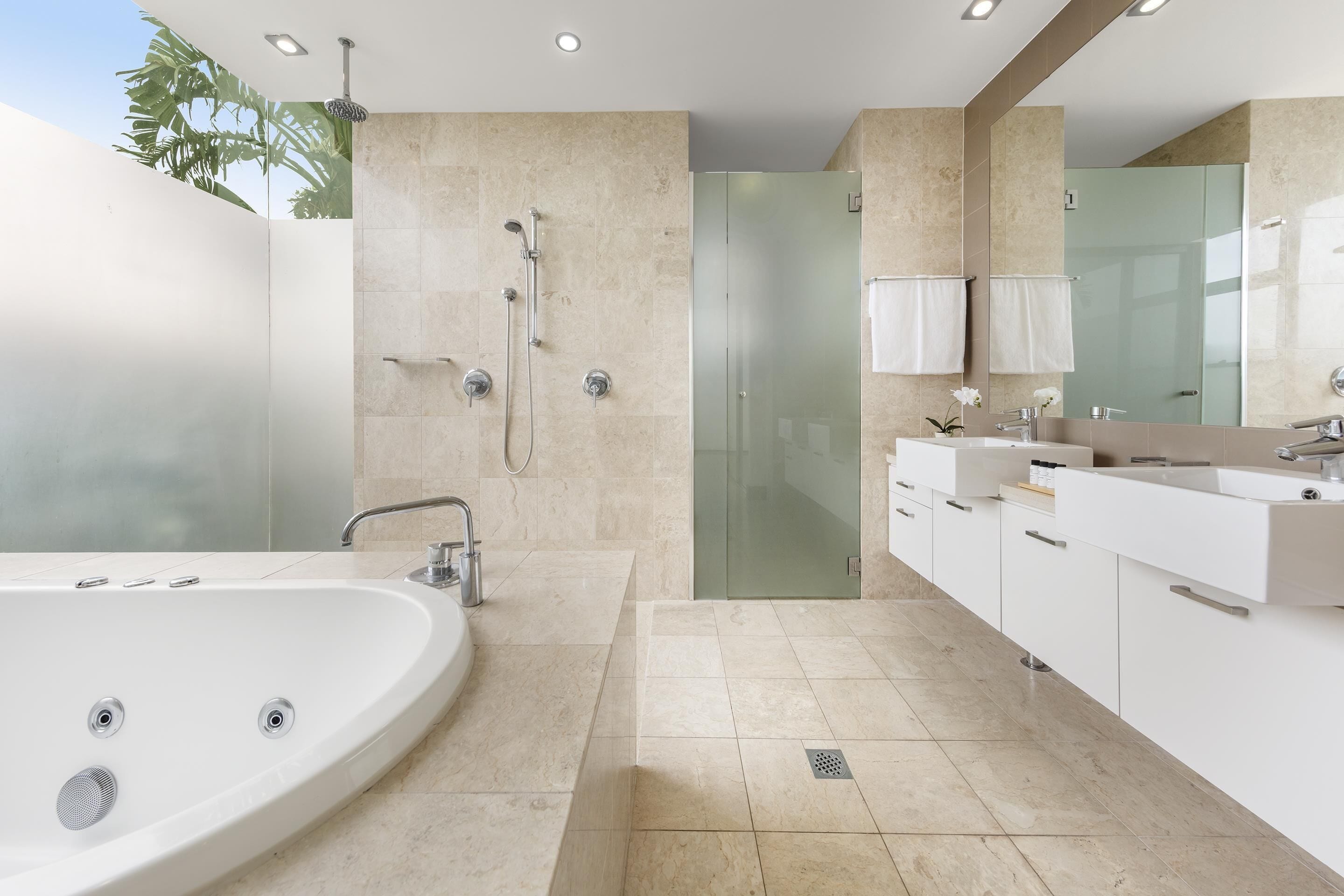Un baño moderno con una bañera grande, cabina de ducha con paredes de vidrio y tocador con espejo.