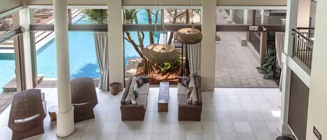 A spacious indoor area with a pool view, featuring multiple seating areas and a hanging light fixture.