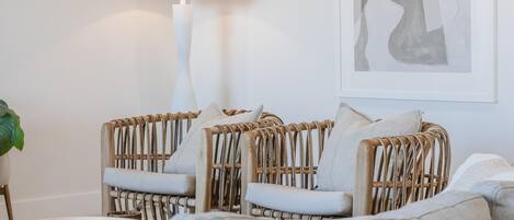 Um quarto com cadeiras de vime, uma mesa redonda de madeira e uma luminária.