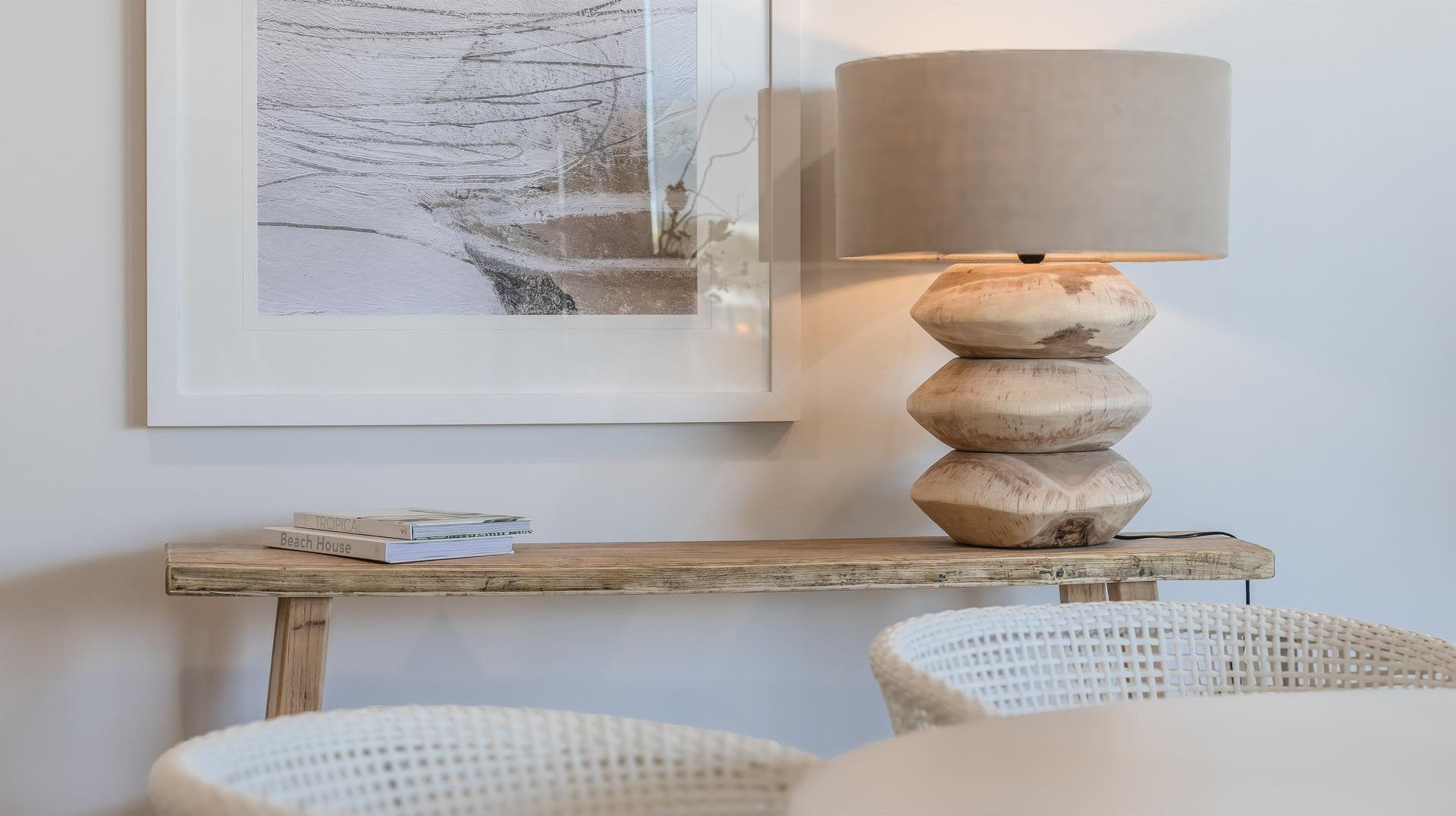 Une lampe posée sur une console en bois, un tableau encadré accroché au mur et deux chaises blanches.