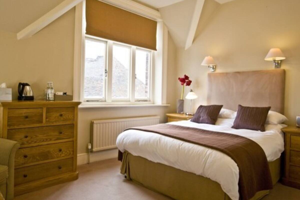 A bedroom with a large bed, a wooden dresser, a window with a view, and two bedside lamps.