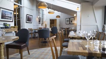 Un restaurante con mesas y sillas de madera, cuadros en las paredes e iluminación colgante.