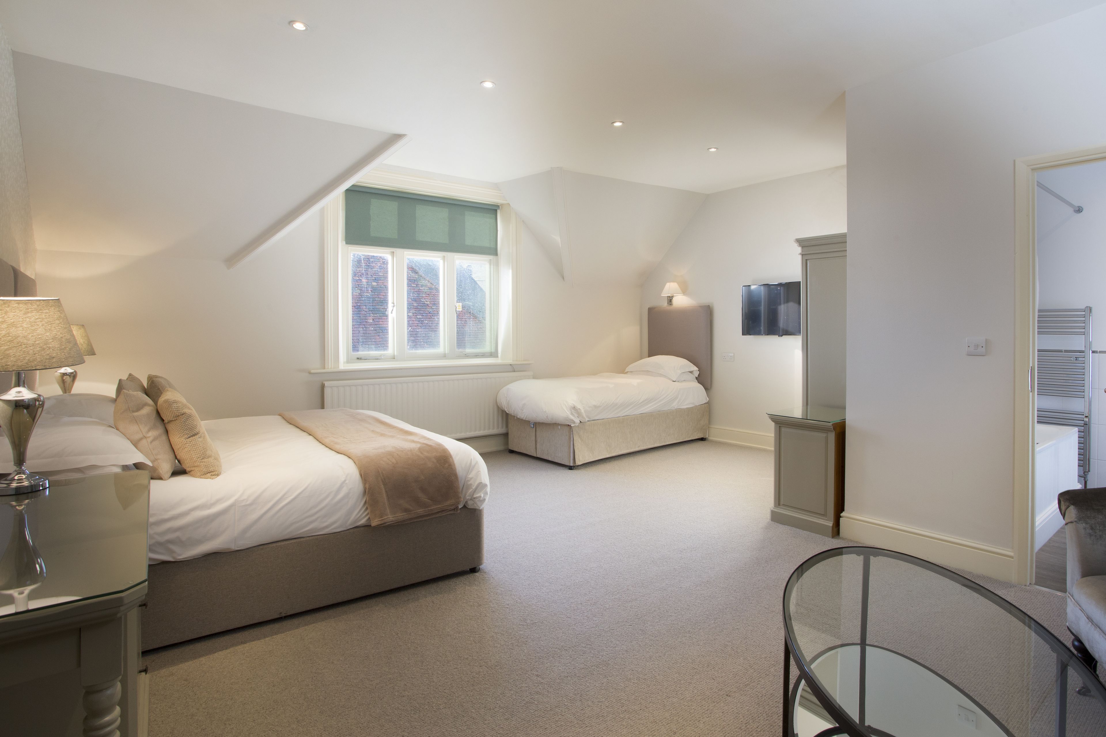 A bedroom with a large bed, a smaller bed, a glass table, and a window with a view of buildings.