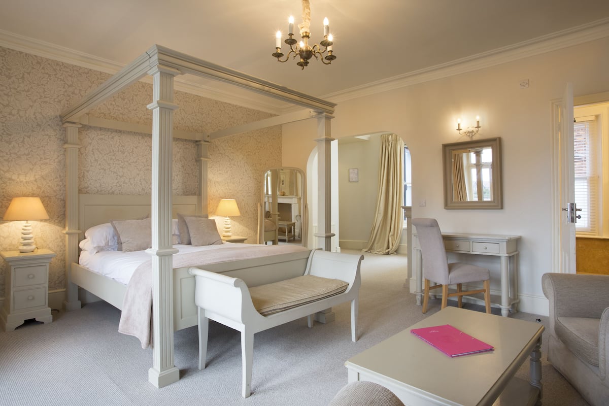 A four-poster bed with a canopy, a desk, a chair, and a bedside table with a lamp.