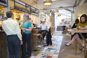 A bar area with wooden stools, a bar counter, and shelves with bottles. - The Bell Hotel (Sandwich)
