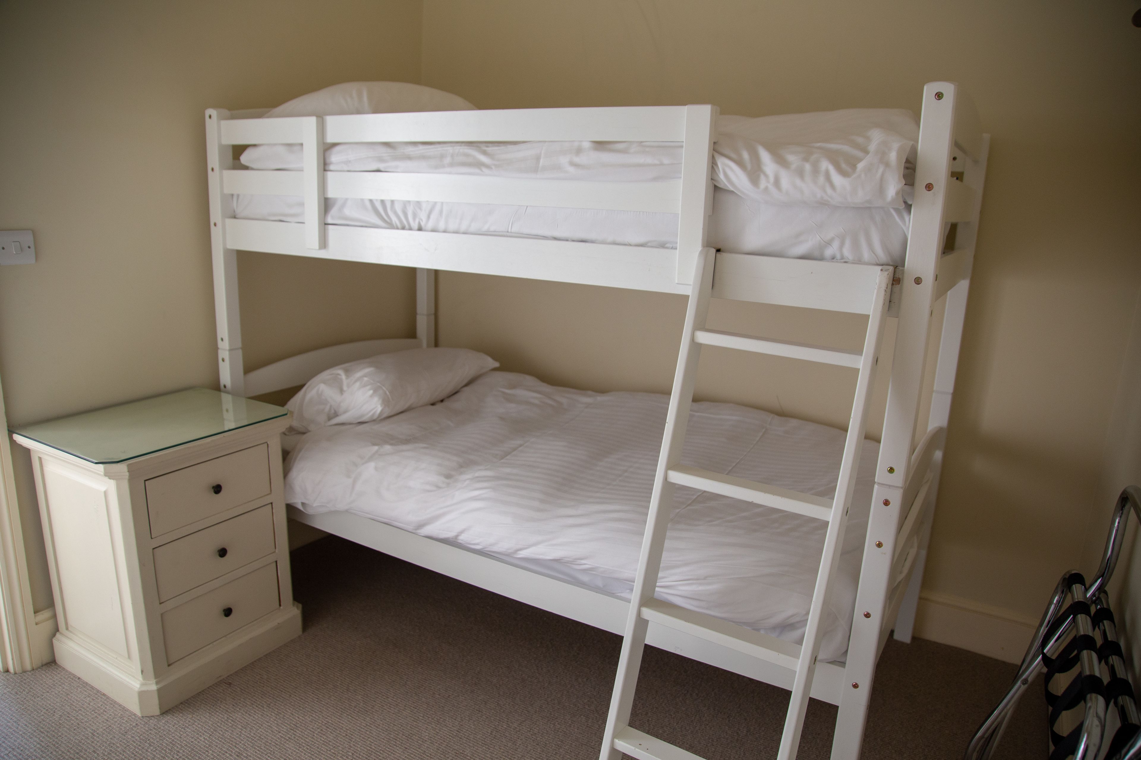 Een stapelbed met een glazen bureau en lades, een ladder en een enkel bed met kussens.