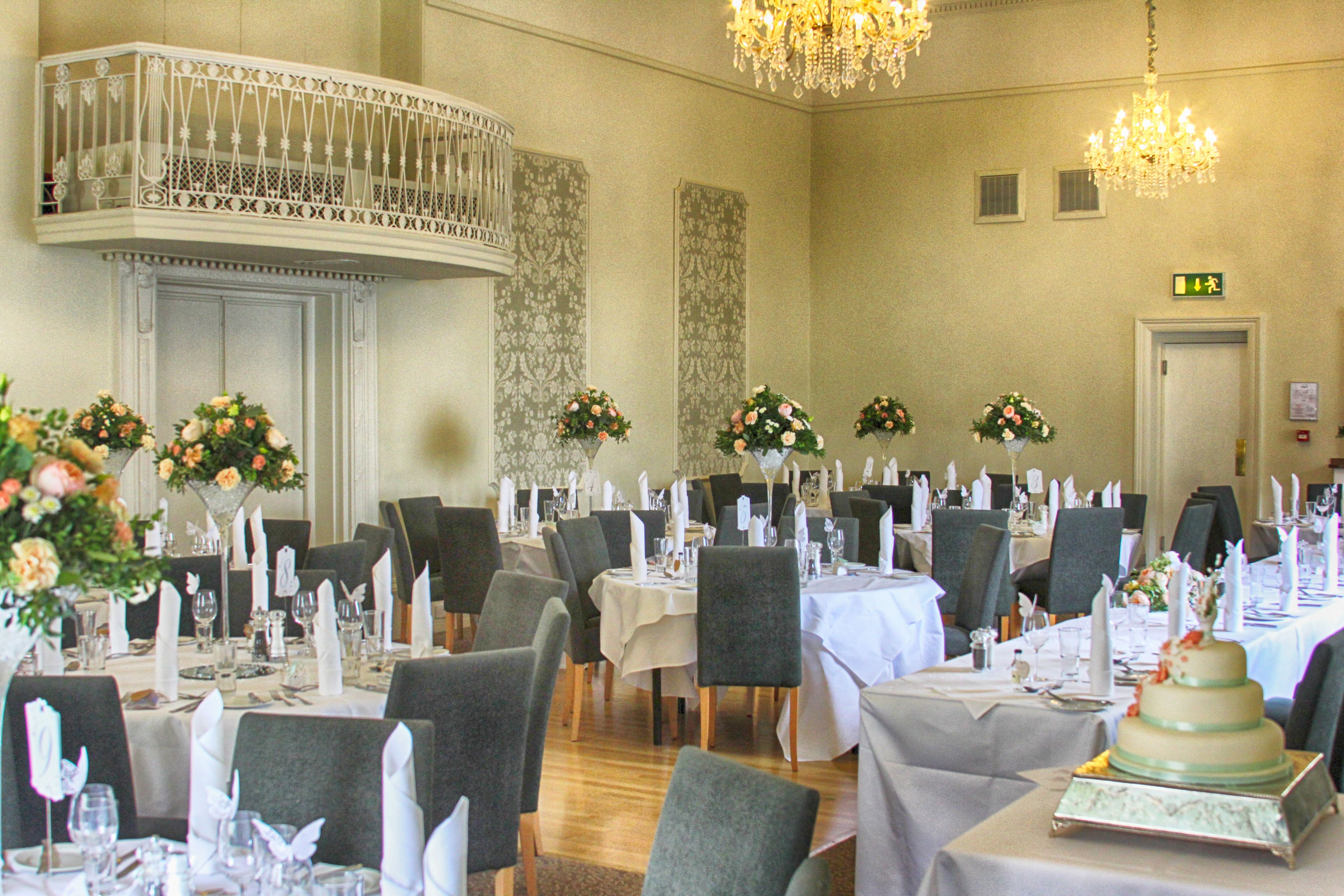 A banquet hall with multiple round tables set for dining, each with white tablecloths and floral centerpieces.