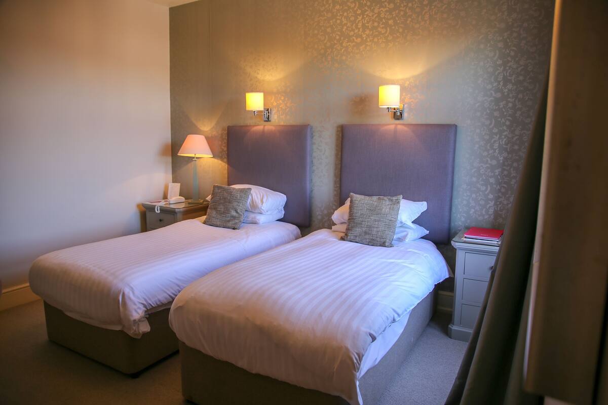 A hotel room with two beds, nightstands, lamps, and a small table with a red book.