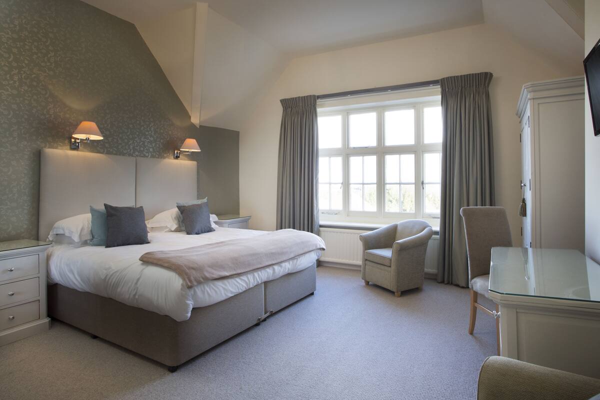 A bedroom with a large bed, bedside tables, a chair, a desk, and a window with curtains.