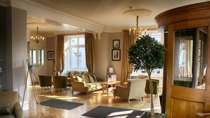 A spacious hotel lobby with a large wooden reception desk, multiple seating areas, and a large indoor plant. - The Bell Hotel (Sandwich)