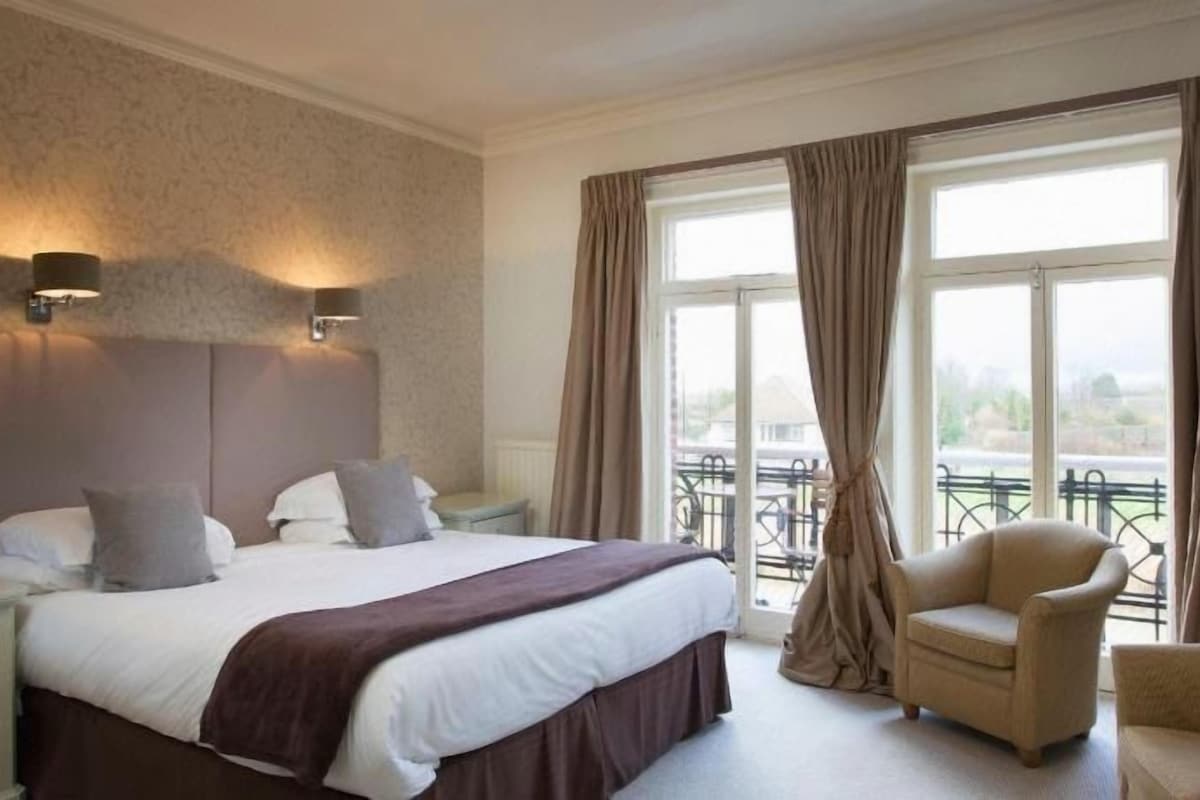 A hotel room with a large bed, bedside lamps, a chair, and a balcony with curtains.