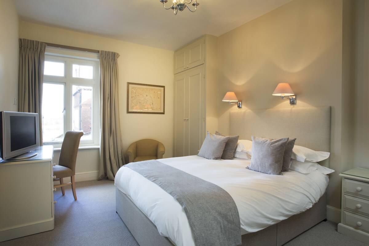 A hotel room with a bed, a desk with a computer, a chair, and two wall-mounted lamps.