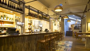 A bar area with wooden bar counter, multiple stools, and a variety of bottles and glasses on shelves. - The Bell Hotel (Sandwich)