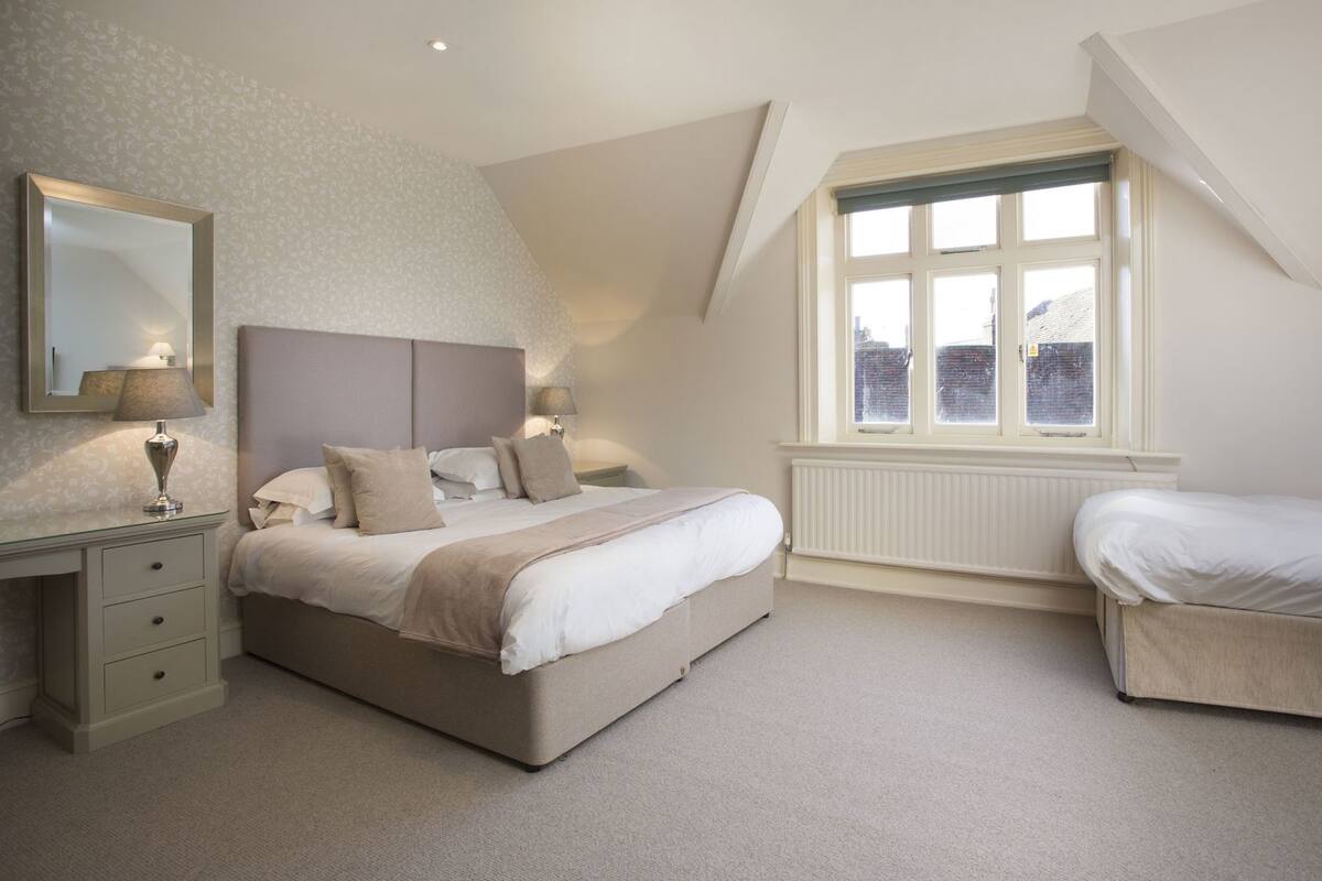 A bedroom with a large bed, bedside tables, a dresser, a window with a view, and a radiator.
