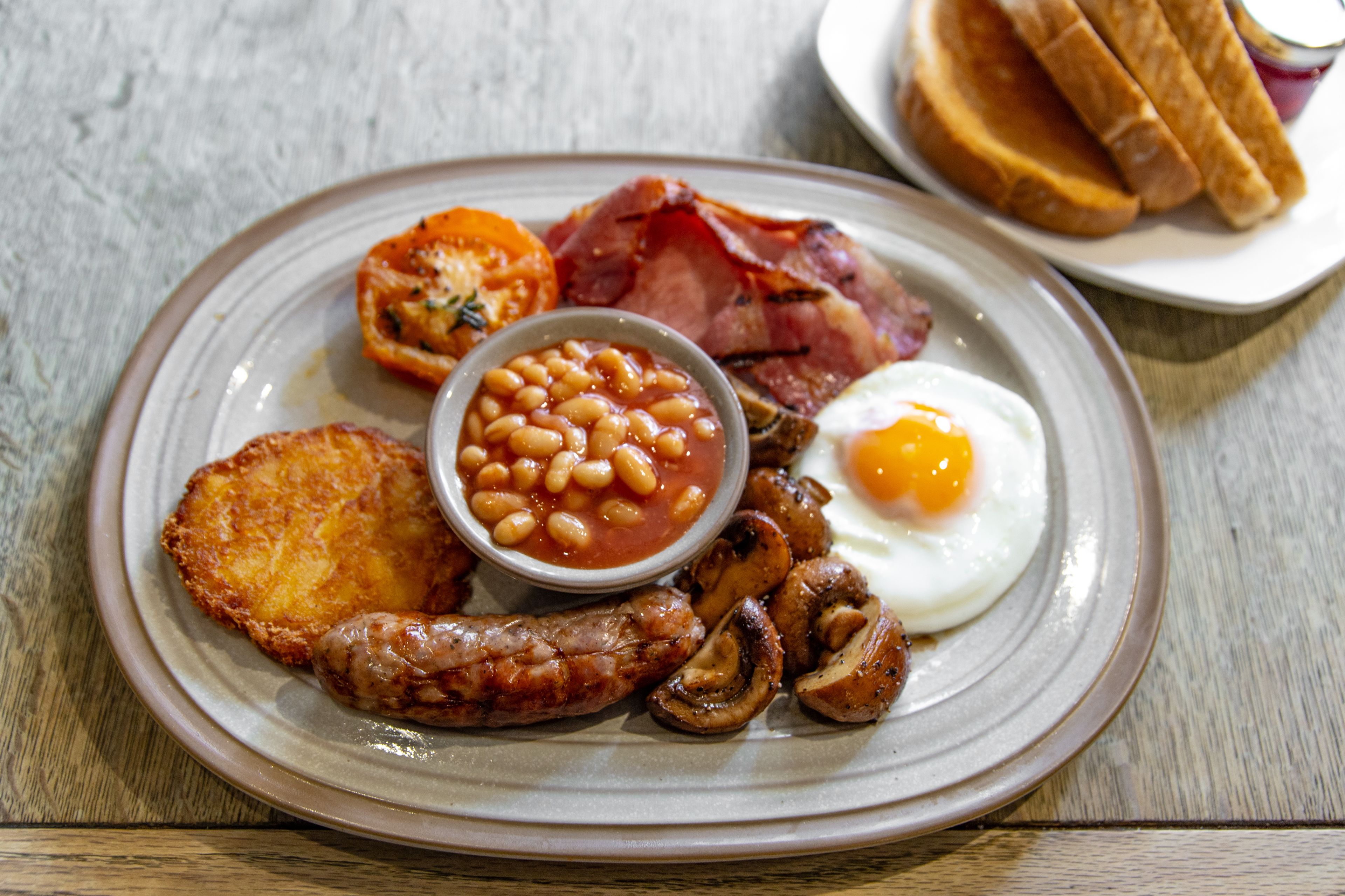 A plate of breakfast food including eggs, bacon, mushrooms, beans, and toast.