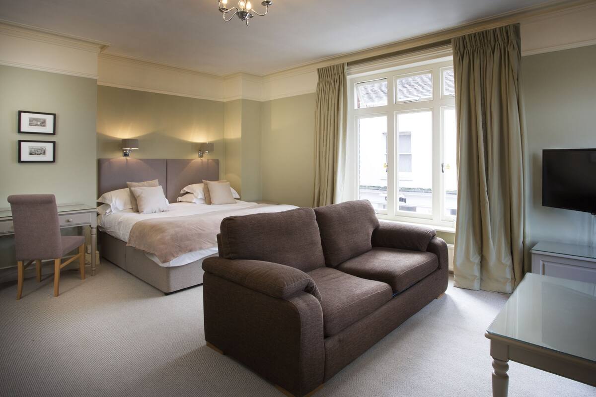 A hotel room with a bed, a sofa, a desk, and a TV.