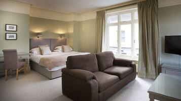 A hotel room with a bed, a sofa, a desk, and a TV.