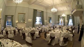 A banquet hall with round tables set for a formal event, chandeliers, and a balcony overlooking the room.