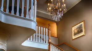 A grand staircase with a wooden handrail and white balusters, leading to a second-floor landing with a chandelier. - The Bell Hotel (Sandwich)