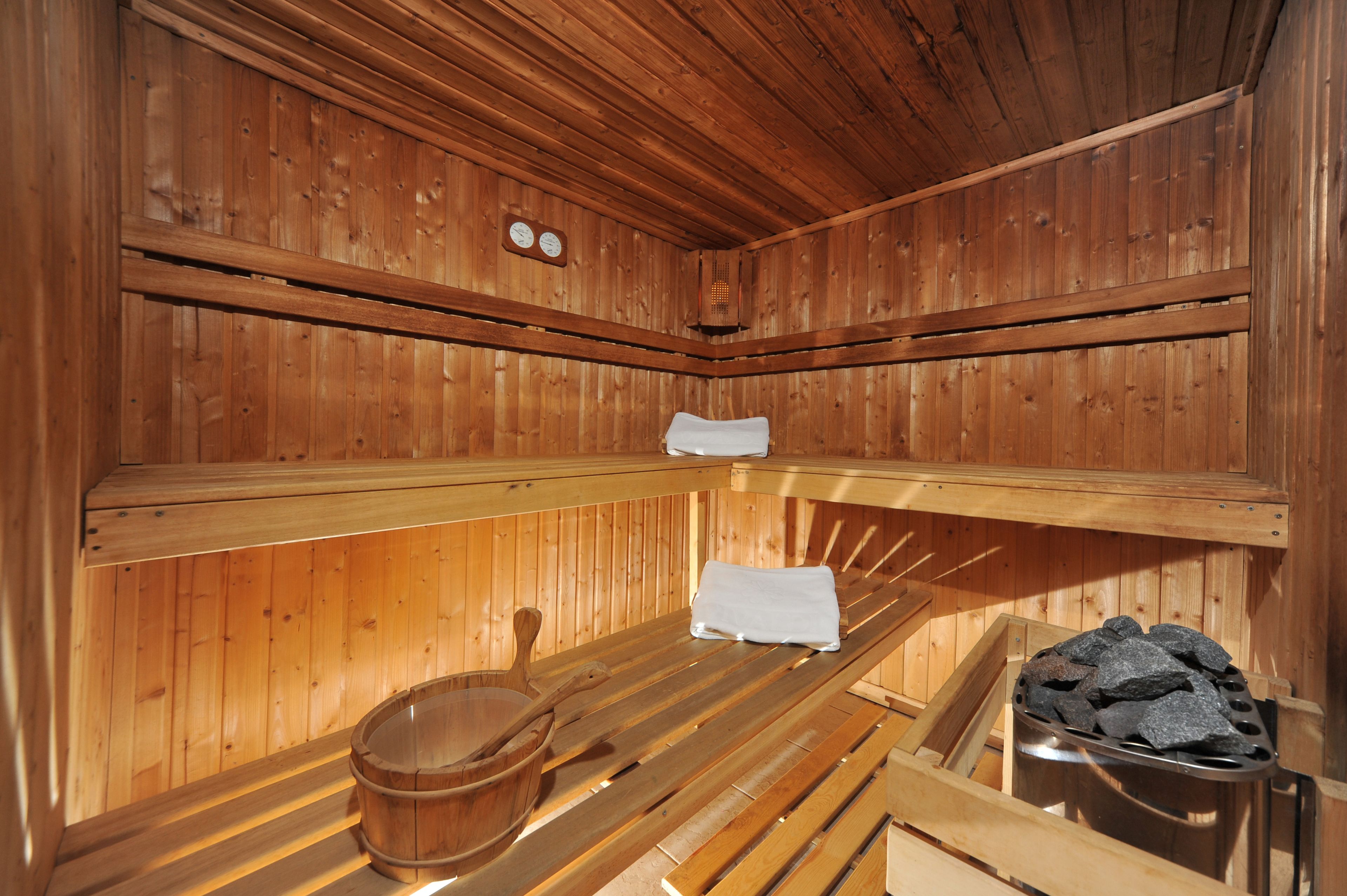 A wooden sauna with benches, a wooden bucket, and a stone heater.
