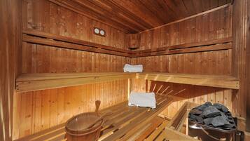A wooden sauna with benches, a wooden bucket, and a stone heater.