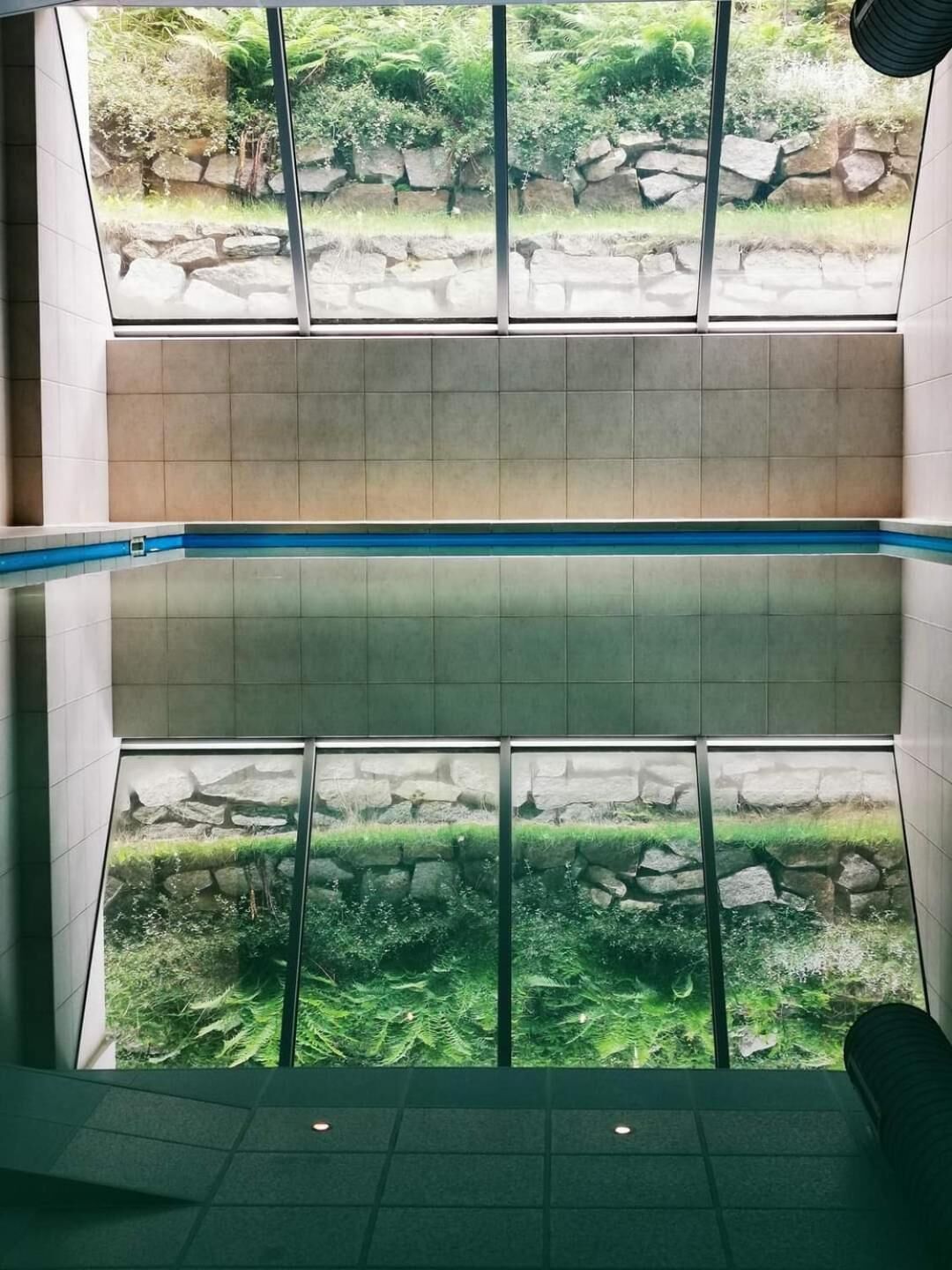 Un intérieur à plusieurs niveaux offrant une vue sur un jardin extérieur grâce à de grandes fenêtres.