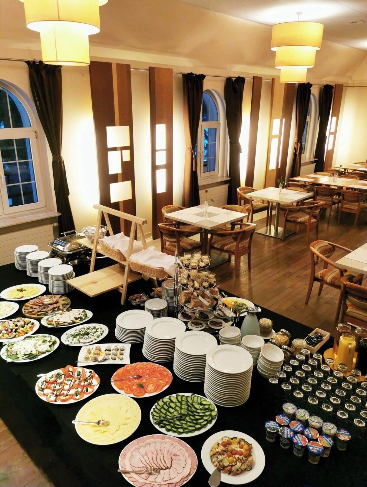 Ein Essbereich mit mehreren Tischen und Stühlen, ein Buffet mit verschiedenen Speisen und ein Fenster mit Vorhängen.