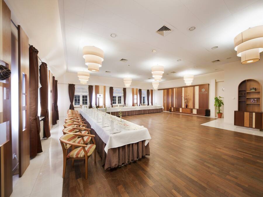 Ein großer Konferenzraum mit einem langen Tisch, Holzstühlen und modernen Leuchten.