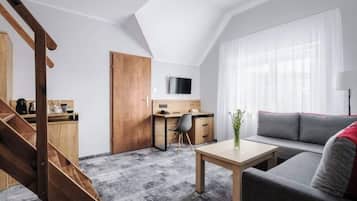 A modern apartment with a loft-style ceiling, a wooden staircase, a dining area, a living room with a sofa, and a kitchen area.