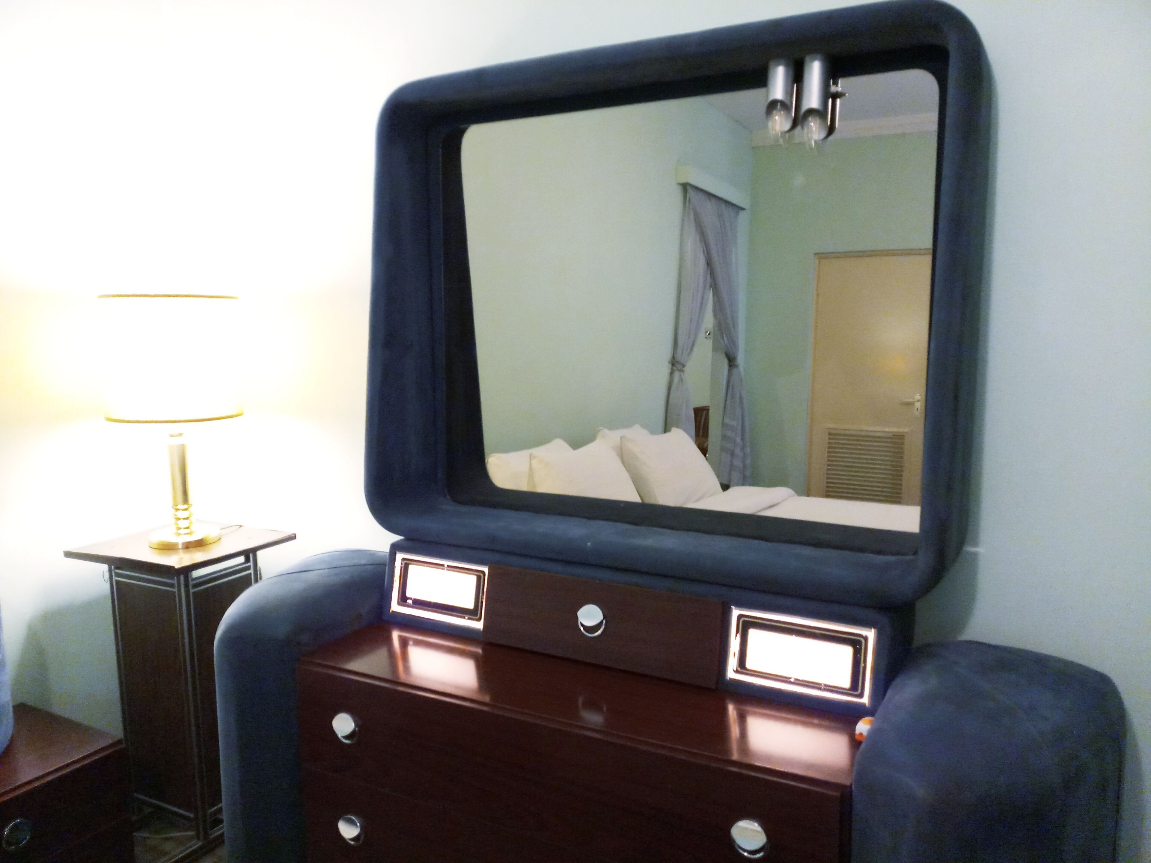 A room with a bed, a dresser with drawers, a lamp, and a mirror on the wall.