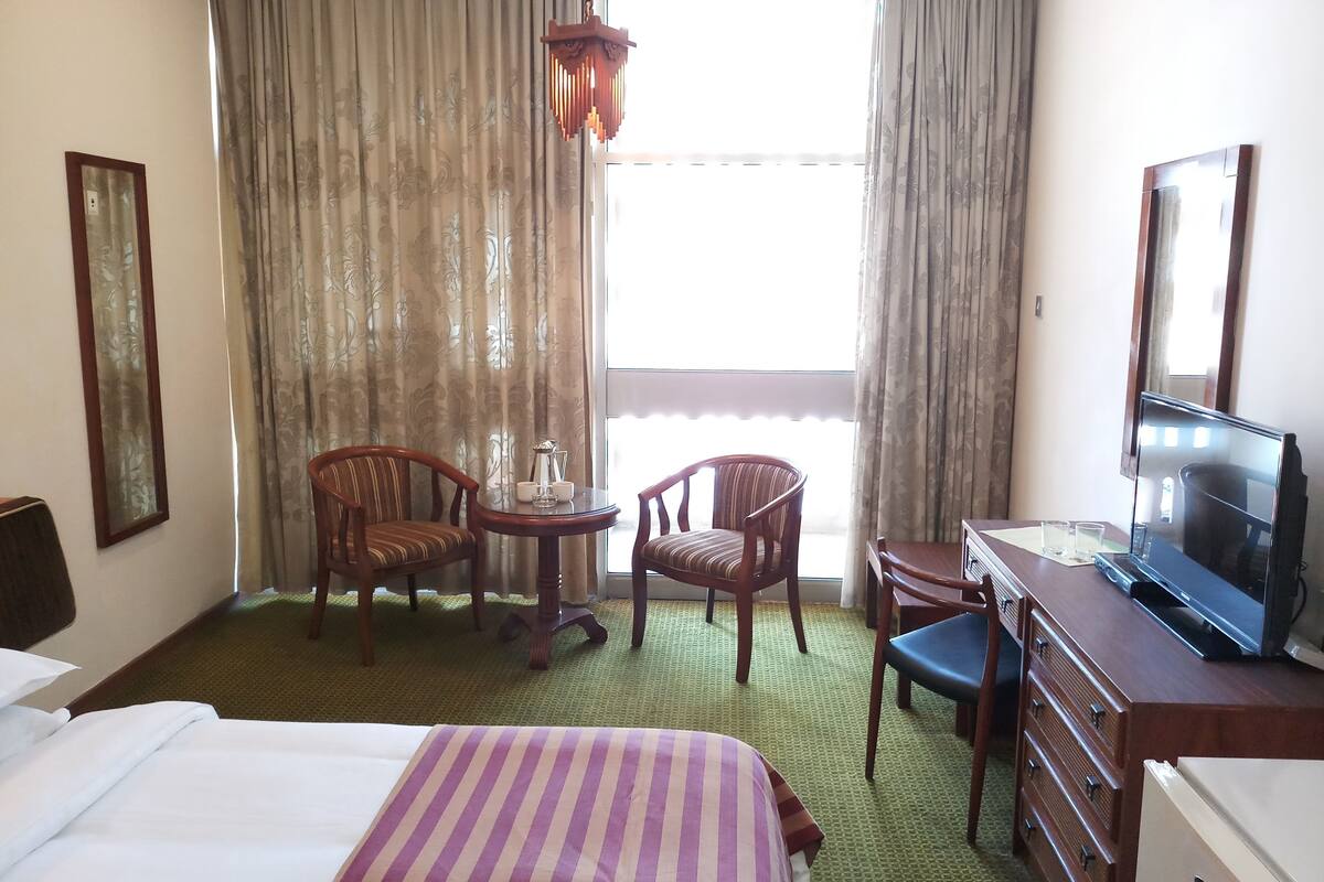 Een hotelkamer met een bed, twee stoelen, een klein tafeltje met een theepot, een televisie en een dressoir.