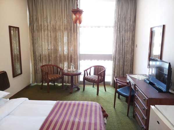A hotel room with a bed, two chairs, a small table with a teapot, a television, and a dresser.