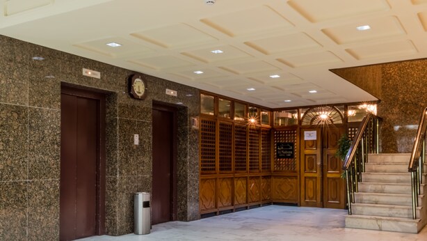 Um hall com piso de mármore, portas de madeira, um relógio e uma escadaria.