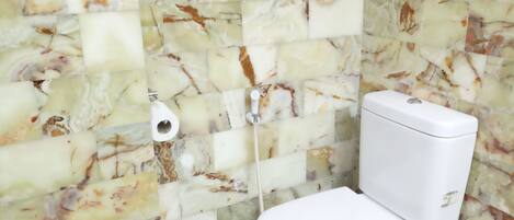 Un baño con inodoro, paredes con diseño de mármol y un dispensador de papel higiénico a la vista.